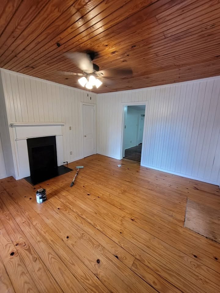 Finished room with restored wood floor, paneled walls, ceiling, and fireplace