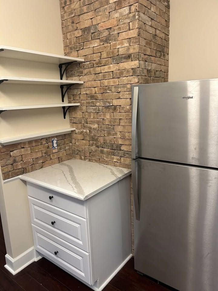 Kitchen work area with brick backsplash, open shelves, cabinetry, and a quartz counter