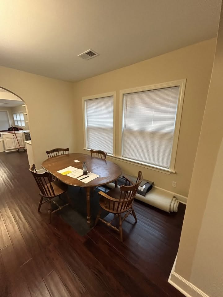 Dining area with finished wood flooring, painted walls, and trimmed windows beside the kitchen