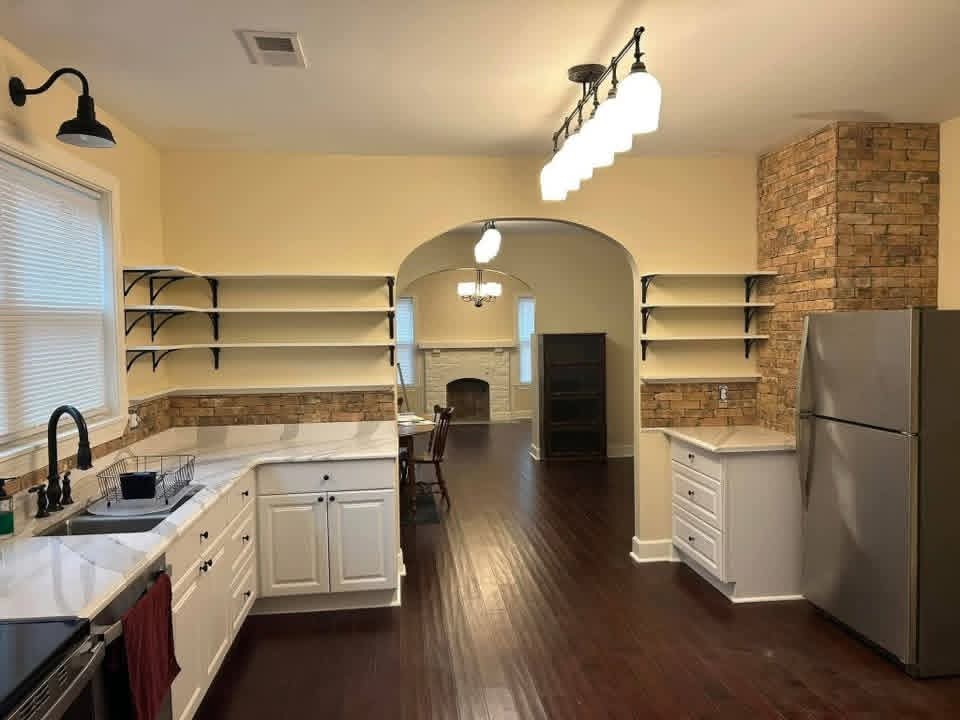 Kitchen with open shelves, brick wall, and archway into the living room
